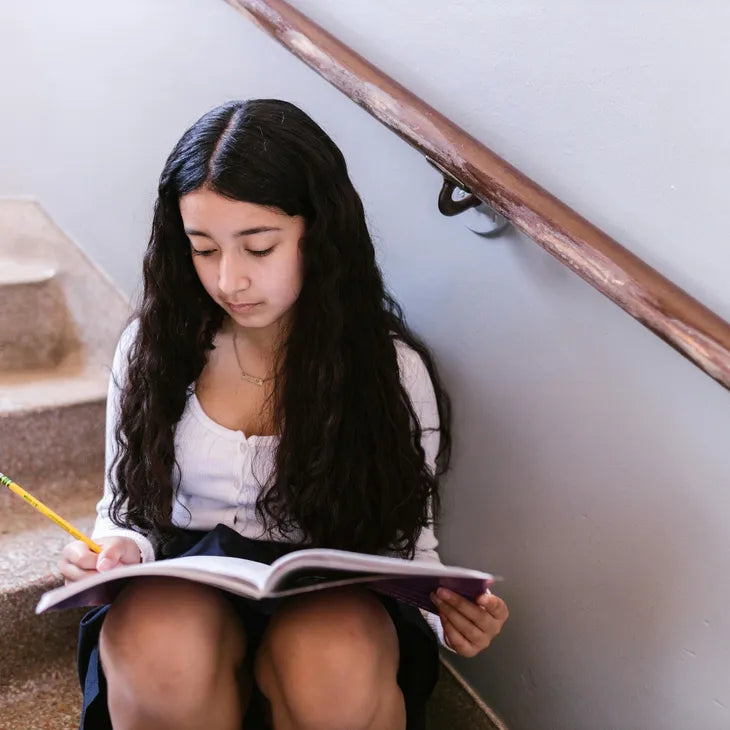 Girl teen sitting on stairs reading a book with a pencil