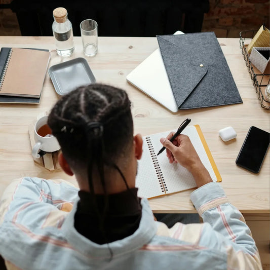 Teen sitting at a desk with a notebook and pen, surrounded by office supplies.