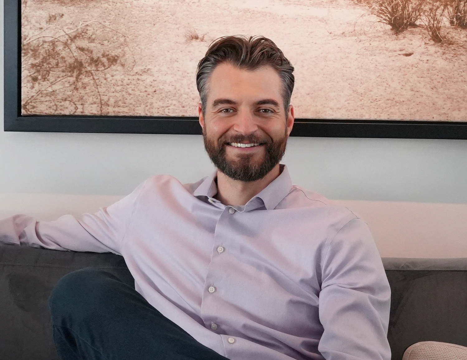 Mentor Drew Sears sitting on a couch wearing a light purple shirt with a map in the background